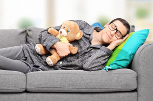 Young man in pajamas sleeping on sofa at home with teddy bear